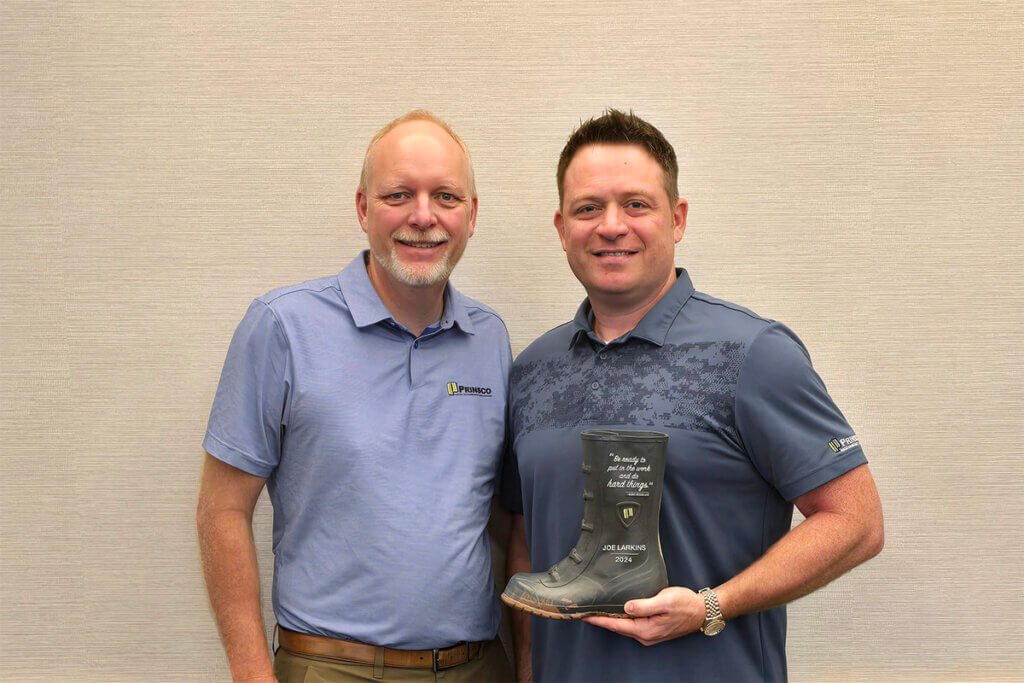 Two men in blue polo shirts posing with a boot award
