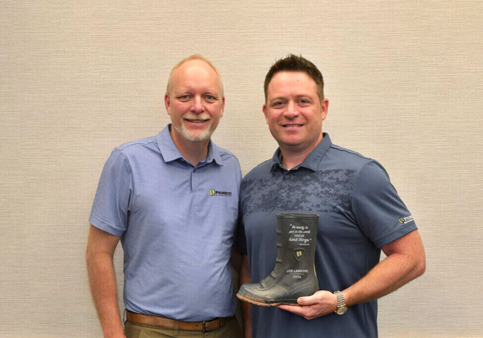 Two men in blue polo shirts posing with a boot award